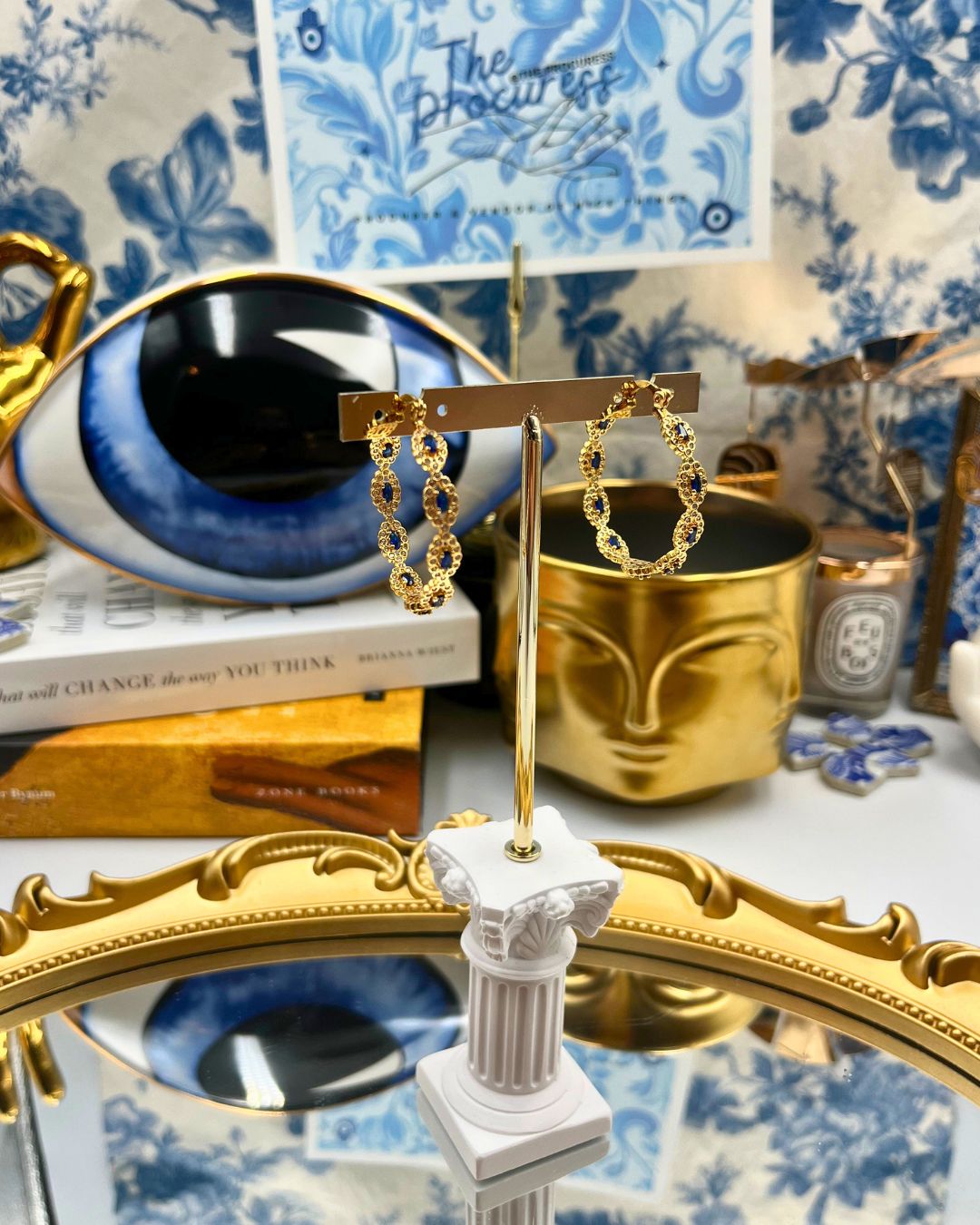 CRYSTAL HAZE Evil Eye Hoops displayed in a decorative still life