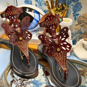 Brown leather butterfly gladiator sandals displayed among objects in The Procuress' Salon
