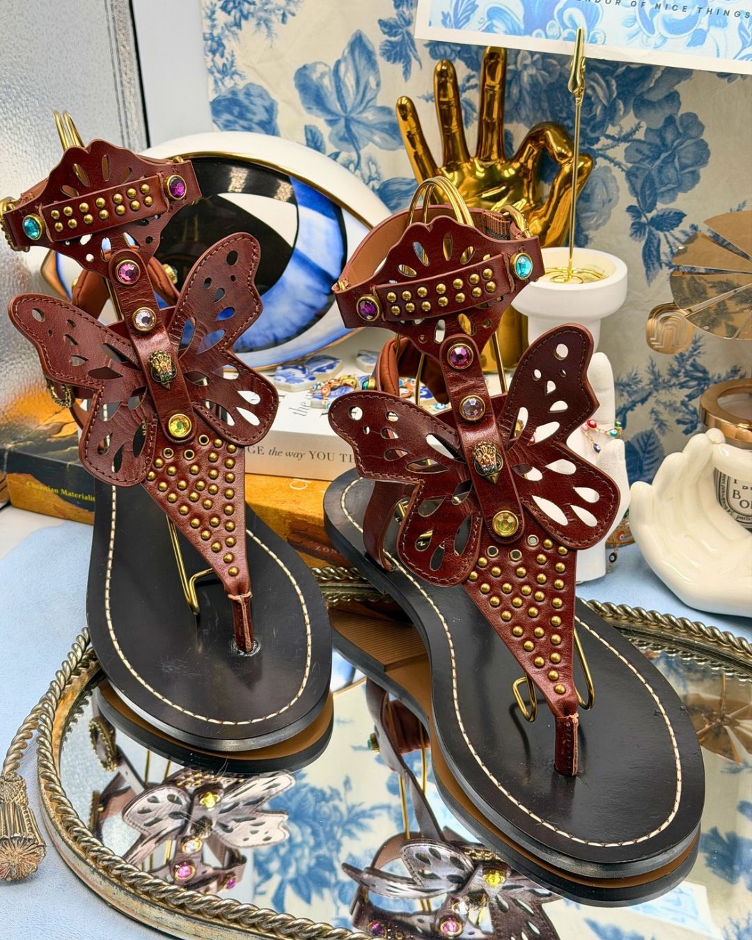 Brown leather butterfly gladiator sandals displayed among objects in The Procuress' Salon