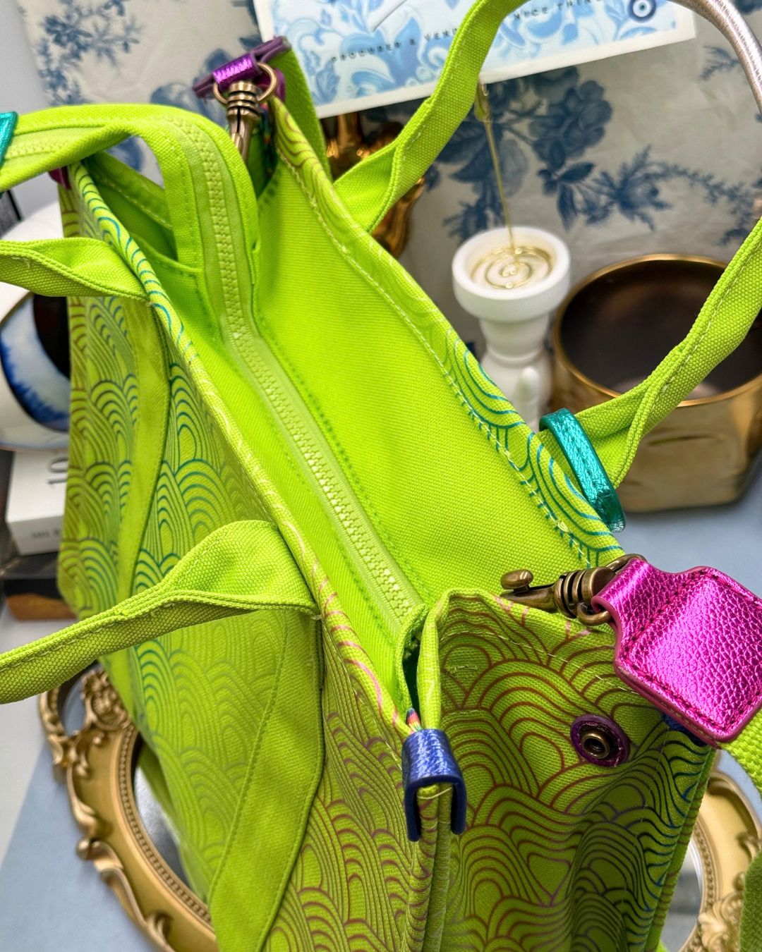 View of zipper of Side view of KURT GEIGER LONDON Southbank Tote Bag in lime canvas with rainbow print wide side poppers released